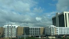 a large white building sitting next to a lush green field under a cloudy blue sky