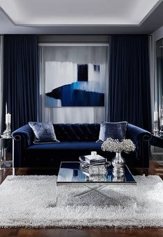 Create an opulent modern living room featuring deep navy and silver tones. Use a plush navy blue sofa as the focal point, surrounded by high-end silver accessories such as a mirrored coffee table, metallic silver vases, and contemporary candle holders. Large floor-to-ceiling windows should allow light to highlight the intricate silver detailing on the furniture. The walls could feature a large, elegant blue-and-silver abstract painting. Add Silver Vases, Navy Blue Sofa, Silver Vase, Blue Sofa