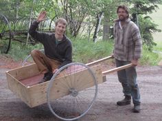 two men standing next to each other near a wooden cart