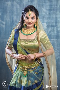 a woman in a green and blue sari is posing for the camera with her hands on her hips