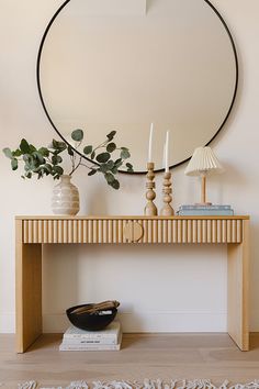 a table with a mirror, vases and candles on it in front of a white wall