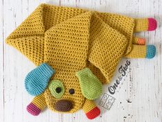 a crocheted yellow dog hat on top of a white wooden floor with colorful buttons