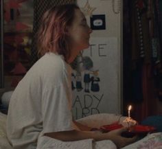 a woman sitting in bed holding a plate with a cake on it and a lit candle