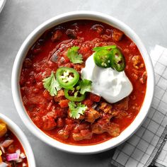 two bowls of chili with sour cream and jalapeno peppers on the side