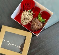 two chocolate covered strawberries in a box with a red rose on the table next to it