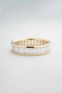 a yellow gold band with baguets and diamonds on the side, set against a white background