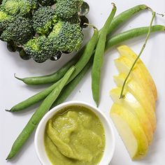 broccoli and green beans are on a cutting board next to a bowl of dip