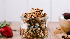 a glass jar filled with granola sitting on top of a wooden table next to strawberries