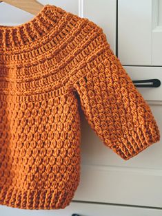 an orange knitted sweater hanging on a white cabinet door with black handles and wooden hangers