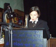 a woman standing at a podium in front of a microphone with words written on it