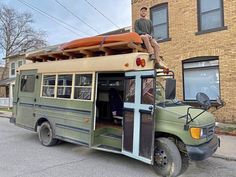 a man standing on top of a green bus with surfboards strapped to it's roof