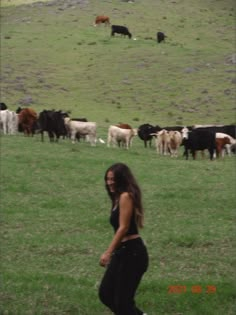 a woman is walking in the grass with cows behind her on a hill side area