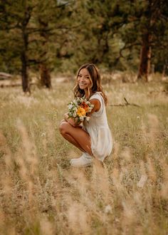 a woman kneeling down in a field with flowers on her hand and smiling at the camera