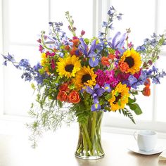 a vase filled with lots of colorful flowers on top of a table next to a cup