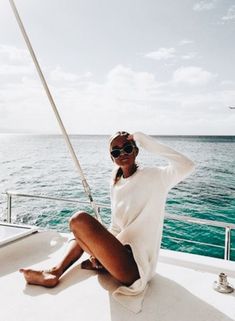 a woman sitting on the back of a boat in the ocean with her legs crossed