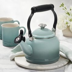 a tea kettle and two mugs sitting on a marble table with white flowers in the background