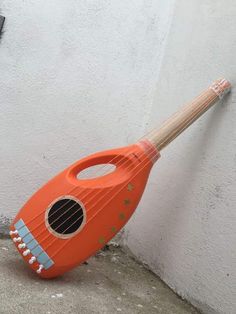 an orange ukulele leaning against a white wall