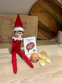 an elf is sitting next to some eggs on the table with a sign that says it's okay