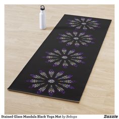 a black yoga mat with purple flowers on it next to a white bottle and pen