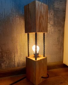 a wooden table lamp with a light bulb on top of it in front of a wall