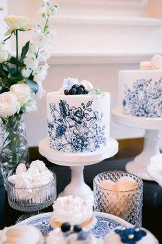 a table topped with two cakes covered in blue and white frosting next to vases filled with flowers