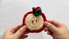 someone is holding up a crocheted apple ornament to show it's face