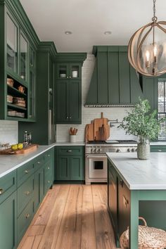 Modern kitchen with green cabinets, white countertops, and wooden floor, featuring a large island with a plant and a decorative light fixture. Green Kitchen Silver Hardware, Green Kitchen Cabinet Inspiration, Artichoke Kitchen Cabinets, Green Kitchen Stainless Steel Appliances, Matte Green Kitchen, Emerald Cabinets Kitchen, Green Color Palette Kitchen, Kitchen Ideas Dark Green, Emerald Green Cabinets Kitchen