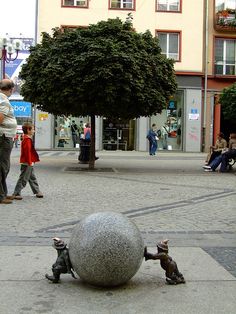 people are walking on the sidewalk near a large ball in the middle of the street