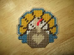 a cross stitch picture of a mouse on a wooden surface