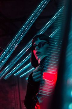 a woman wearing sunglasses standing in front of some neon lights and looking at her cell phone