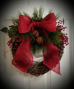 a christmas wreath hanging on the front door with red ribbon and bells attached to it