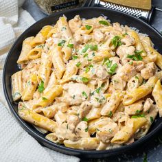 a bowl full of pasta with chicken and parsley on the side next to some bread