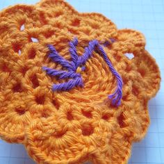 an orange crocheted flower with purple thread