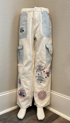 a pair of white jeans with patches and buttons on them, sitting against a wall