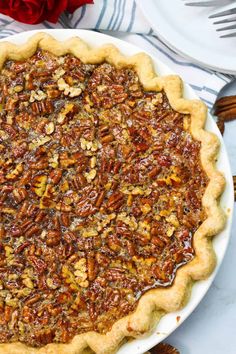 a pecan pie on a white plate with red rose in the background and two forks next to it