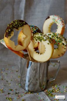 apple slices and sprinkles are arranged in a metal cup on a table