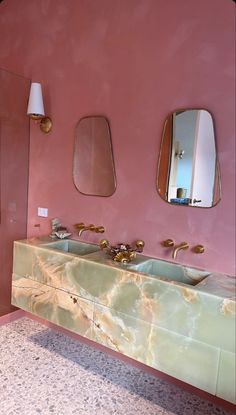 a bathroom with two sinks and mirrors on the wall, in front of a pink wall