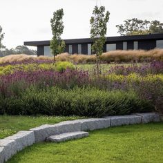 a stone bench sitting in the middle of a lush green field next to a building