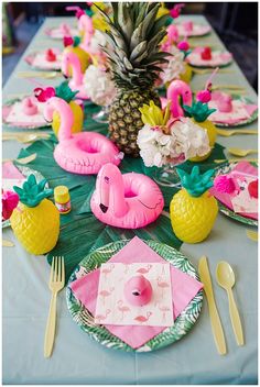 a table topped with pink flamingos and pineapples next to plates and utensils