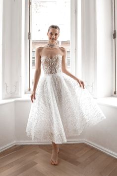 a woman standing in front of a window wearing a white dress