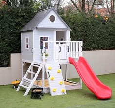 there is a play house with a slide and ladders on the grass in front of it