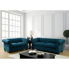 two blue couches sitting next to each other in front of a white wall with windows