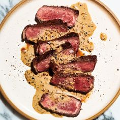 a white plate topped with sliced up meat on top of a marble countertop next to a knife and fork