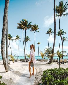 a woman standing on the beach in front of palm trees