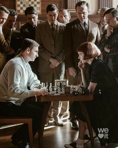 a group of people standing around a table playing chess