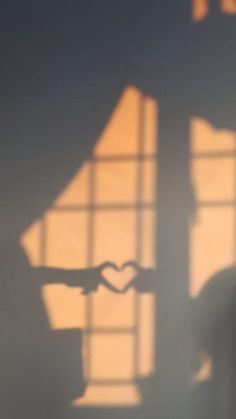 the shadow of a person making a heart sign with their hand in front of a window