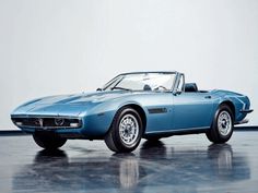 an old blue sports car is parked in a room with a white wall behind it