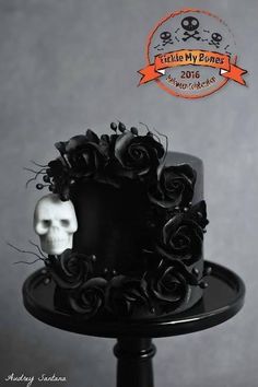 there is a black cake decorated with roses and a skull on the top, in front of a gray background