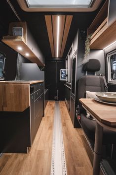 the interior of an rv with wood flooring and black walls, windows, and cabinets