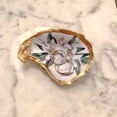 two wedding rings are placed in a decorative bowl on a marble surface with gold trim